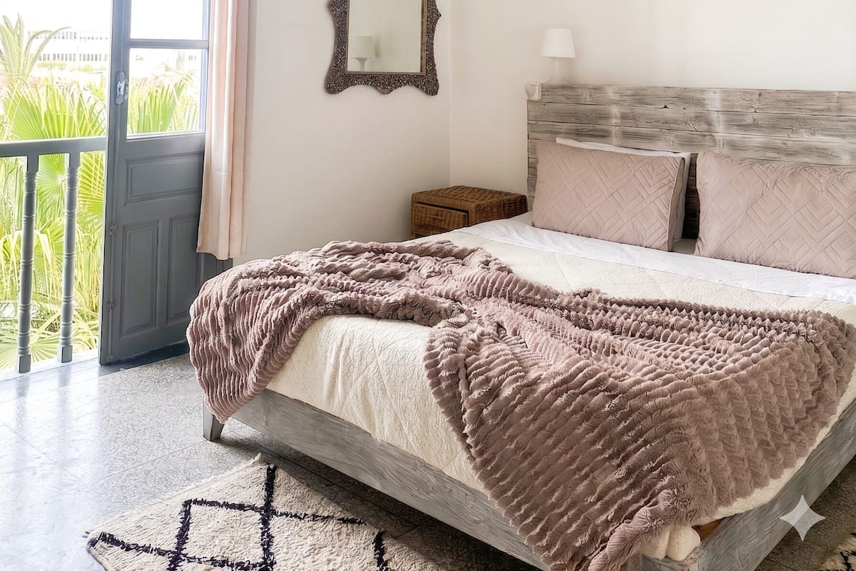 A bedroom with a bed, a hanging light fixture, a mirror, and a painting on the wall.