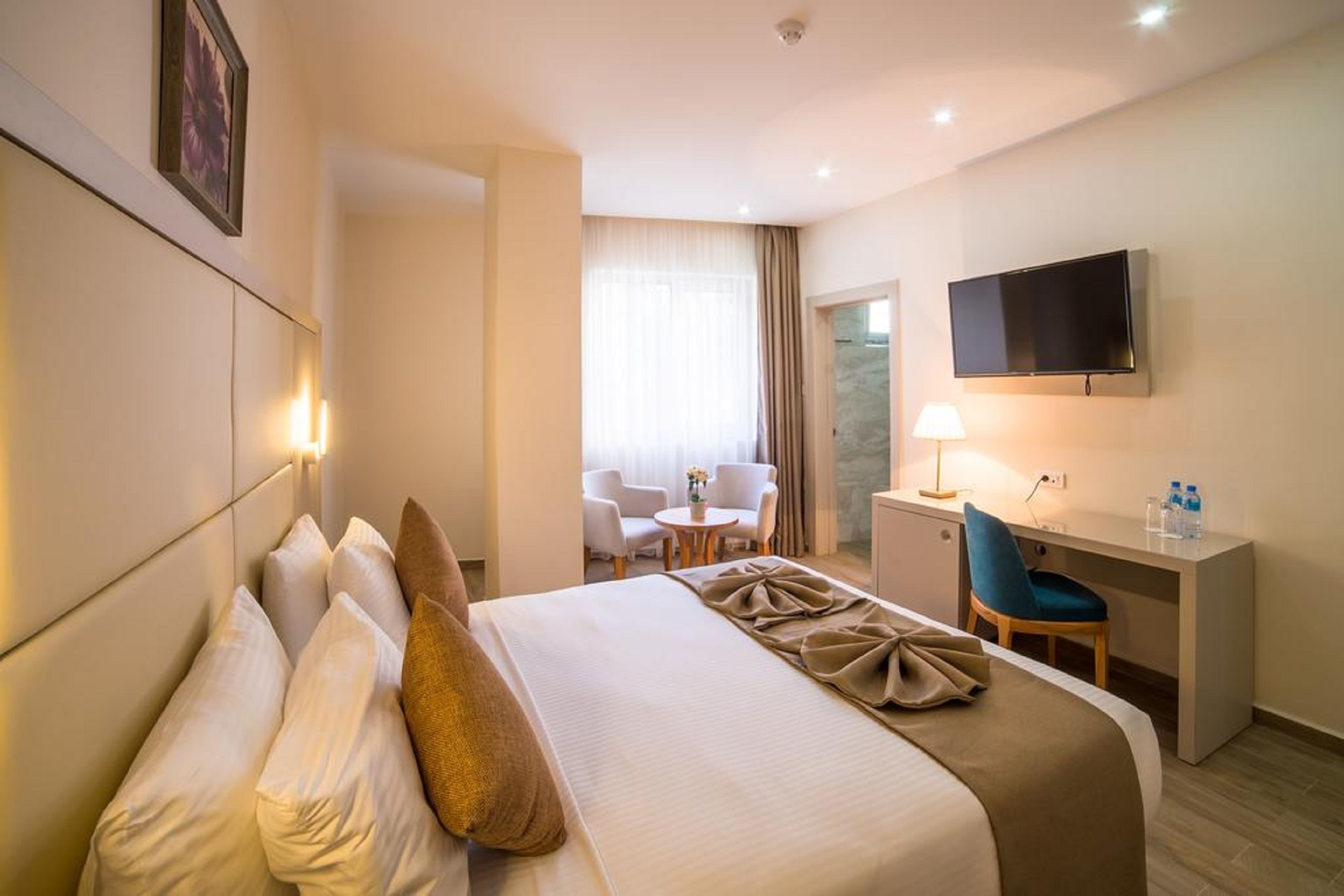 Habitación de hotel con cama, escritorio, silla, televisión y ventana con cortinas.