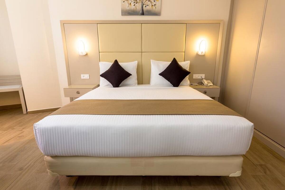 Een hotelkamer met een groot bed, twee nachtkastjes met lampen en een aan de muur bevestigde telefoon.