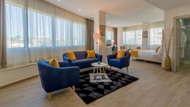 Una habitación de hotel moderna con un ventanal grande, un conjunto de sofás, una cama y una mesita.