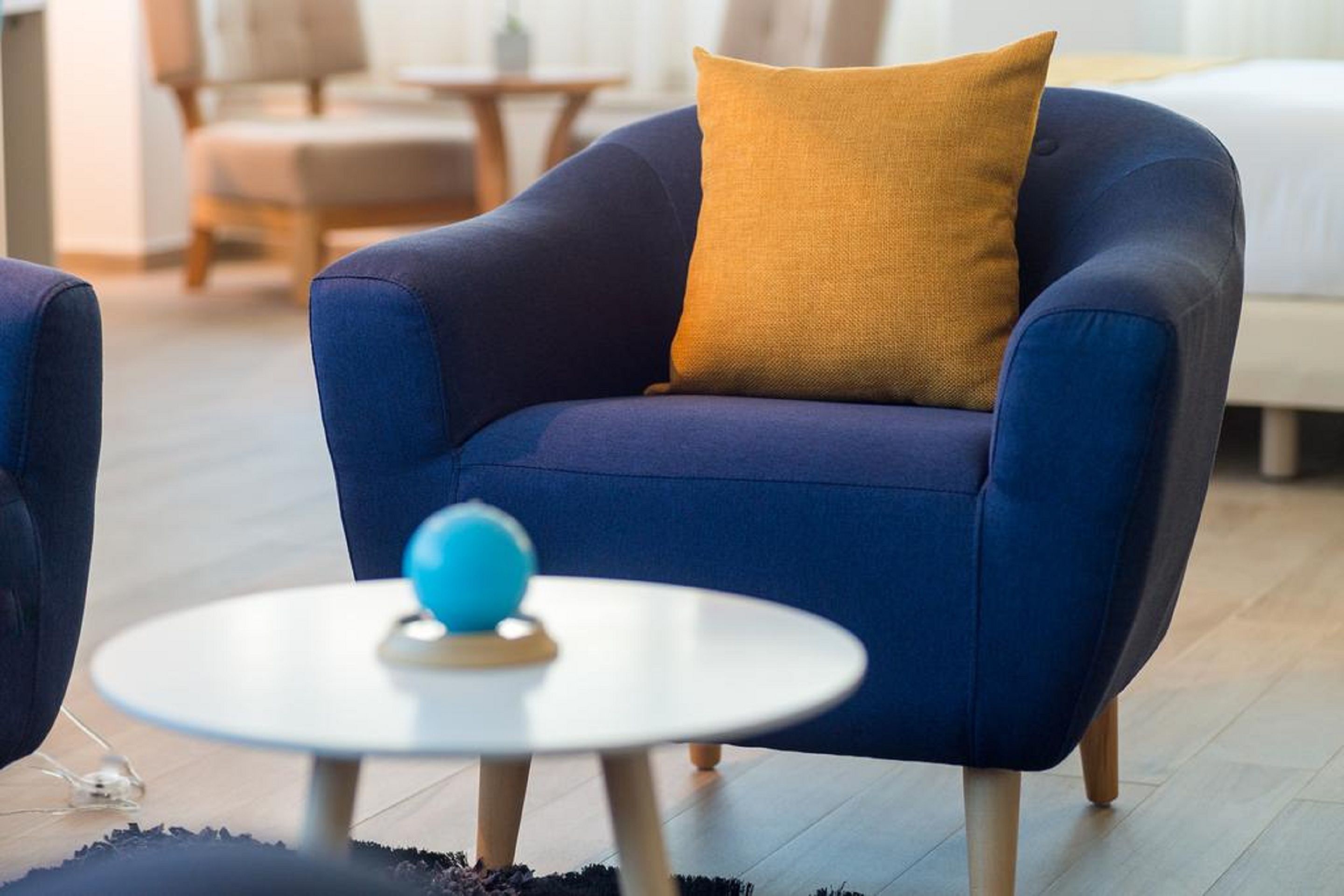 Un salon moderne avec un fauteuil bleu, une table ronde blanche et un coussin de couleur moutarde.