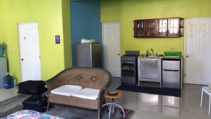 A compact hotel room with a bed, a wicker sofa, a kitchenette, and a bathroom. - Casa Azul Apartment (Puerto Plata)