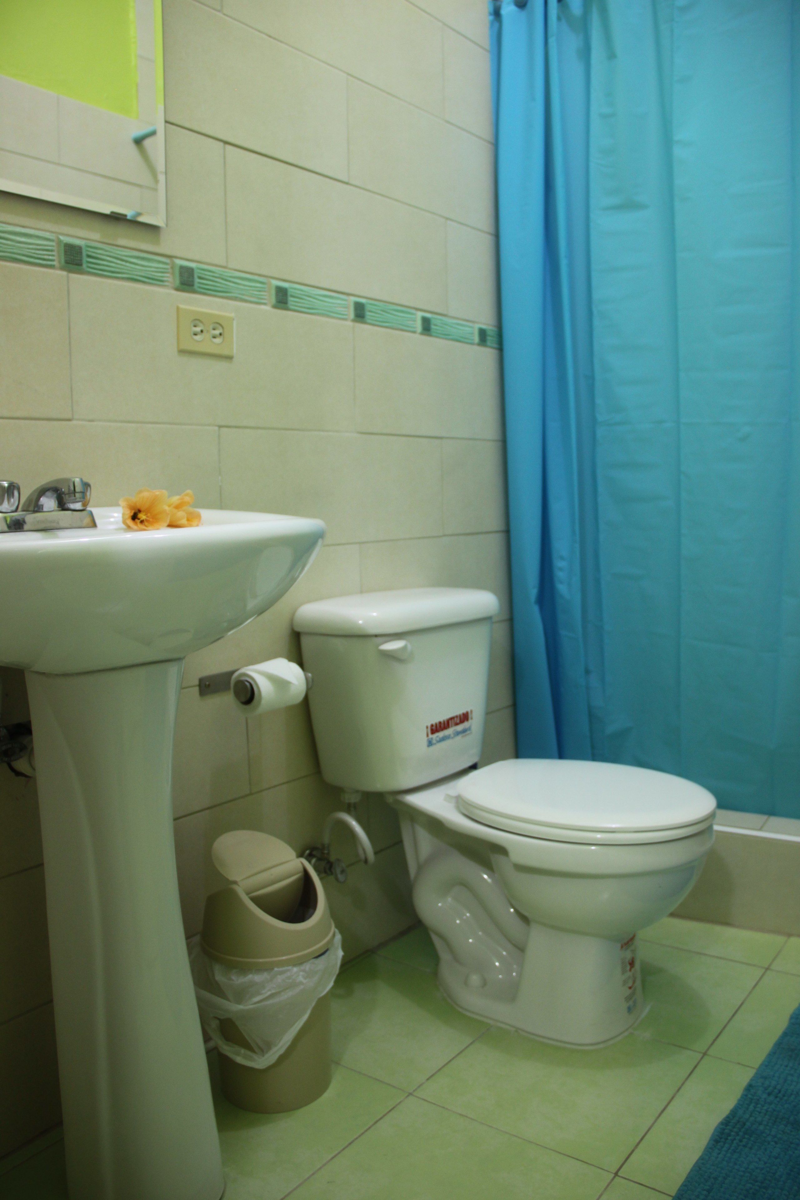 Un baño con lavamanos blanco, inodoro y cortina de ducha azul.
