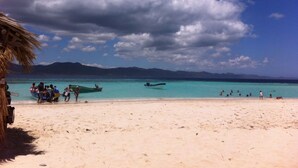 A beach with clear turquoise water, a thatched-roof structure, and boats in the distance. - Casa Azul Apartment (Puerto Plata)