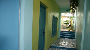A narrow hallway with a blue door, a window with metal bars, and a tiled floor leading to a staircase. - Casa Azul Apartment (Puerto Plata)