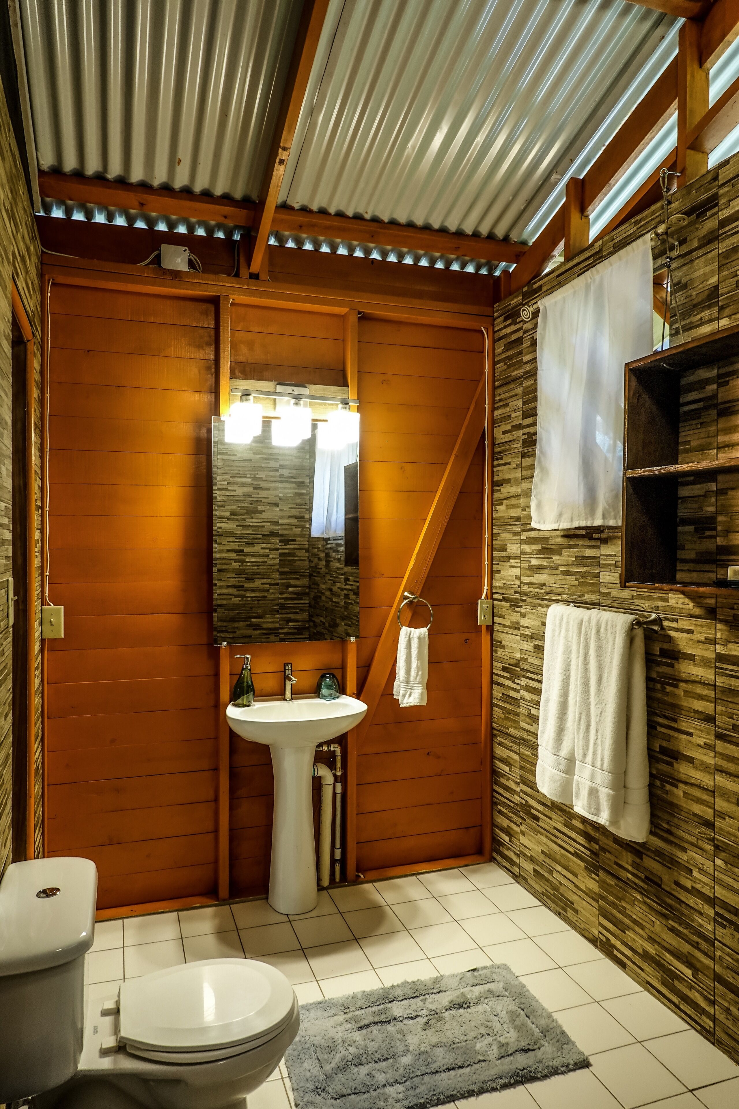 A bathroom with wooden walls, a white sink, a toilet, and a mirror with lights.