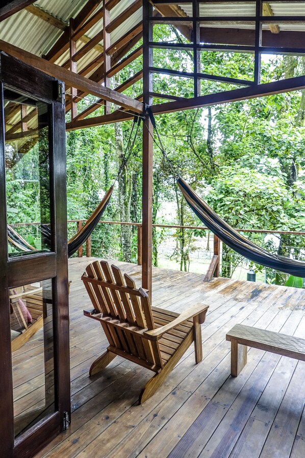 A wooden deck with a hammock, a wooden chair, and a bench.