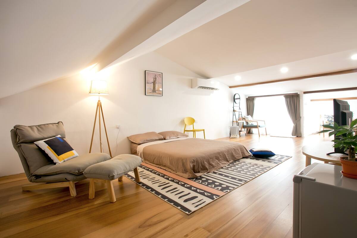 A bedroom with a bed, a chair, a desk, and a potted plant.