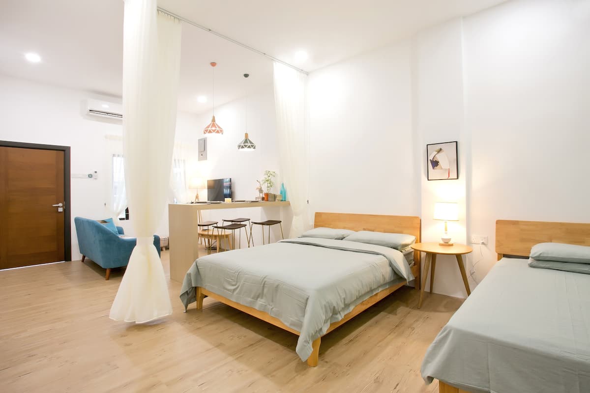 A hotel room with two beds, a desk, a chair, and a small table with a lamp.