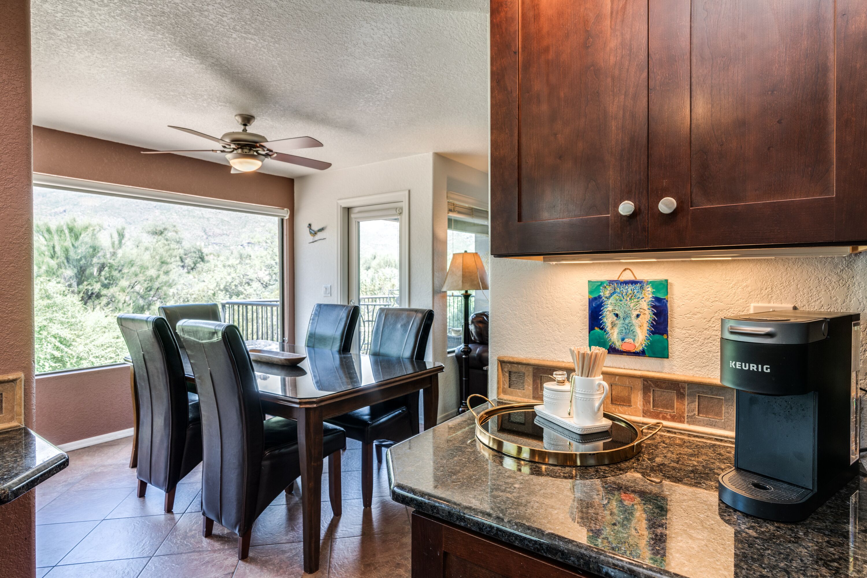 A kitchen with a dining table, chairs, a coffee maker, and a view of the outdoors.