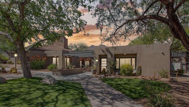 Une maison moderne dotée d’un patio couvert, d’une pelouse bien entretenue et de quelques cactus.