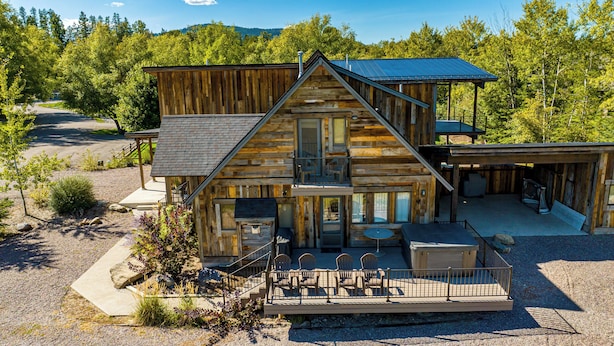 Une cabane en rondins à deux étages, dotée d’un balcon, d’un espace salon extérieur et d’une terrasse couverte.