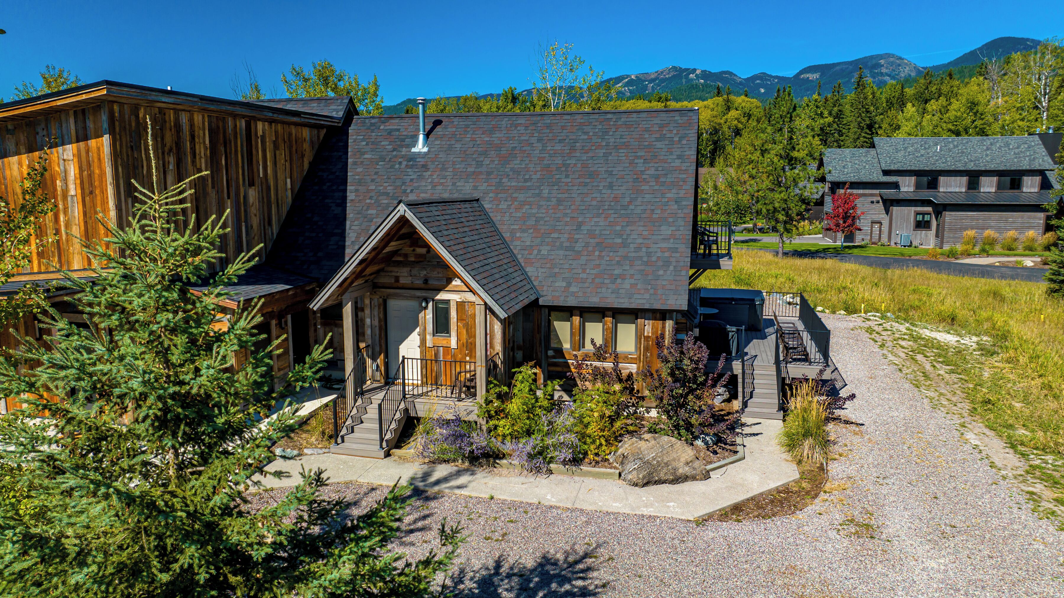 A modern log cabin with a stone roof, a wooden porch, and a gravel driveway.