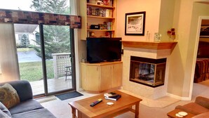 A cozy living room with a fireplace, a television, and a bookshelf. - F48 Modern home with AC within walking distance of golf course and Mt Washington Hotel (Bretton Woods)