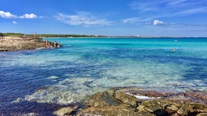A coastal beach scene with clear turquoise water, rocky shore, and distant buildings. - Dimora storica Briganti (Gallipoli)