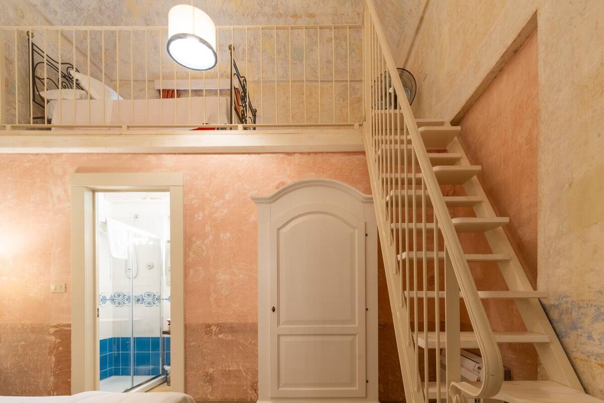 Een slaapkamer met een bed, een kledingkast, een trap en een deur naar een badkamer.