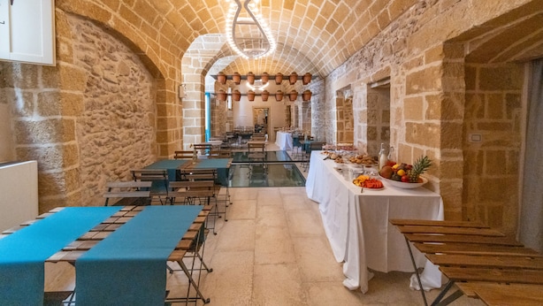 A spacious hall with stone walls, a long table with blue tablecloths, and a central chandelier. - Dimora storica Briganti (Gallipoli)