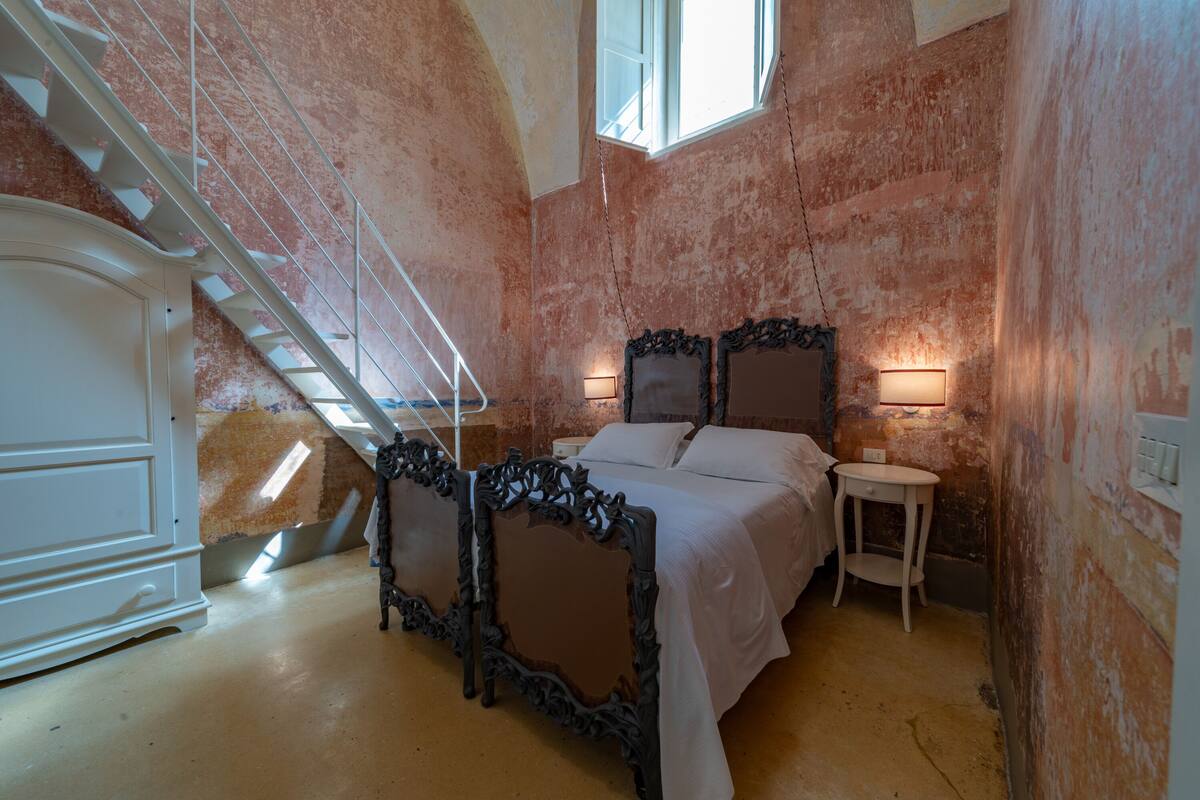 Een slaapkamer met een bed, twee nachtkastjes, een trap en een raam.