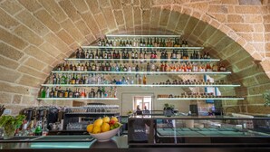 A bar with multiple shelves of bottles and glasses, a bowl of fruit, and a cash register. - Dimora storica Briganti (Gallipoli)