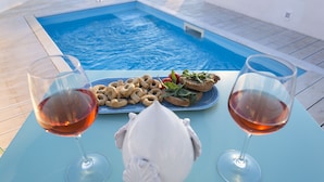 A poolside table with two glasses of red wine, a plate of snacks, and a white shell-shaped object. - Dimora storica Briganti (Gallipoli)