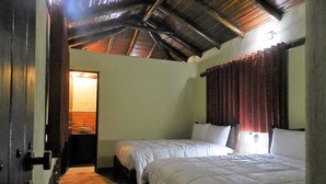 Un dormitorio con dos camas, vigas de madera en el techo, un baño pequeño y una puerta que da a otra habitación.