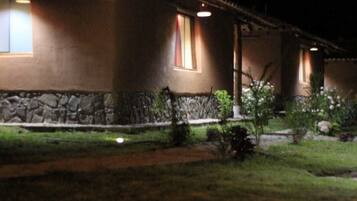 Una casa con base de piedra y techo de tejas. Se ven dos ventanas con luces encendidas en el interior.