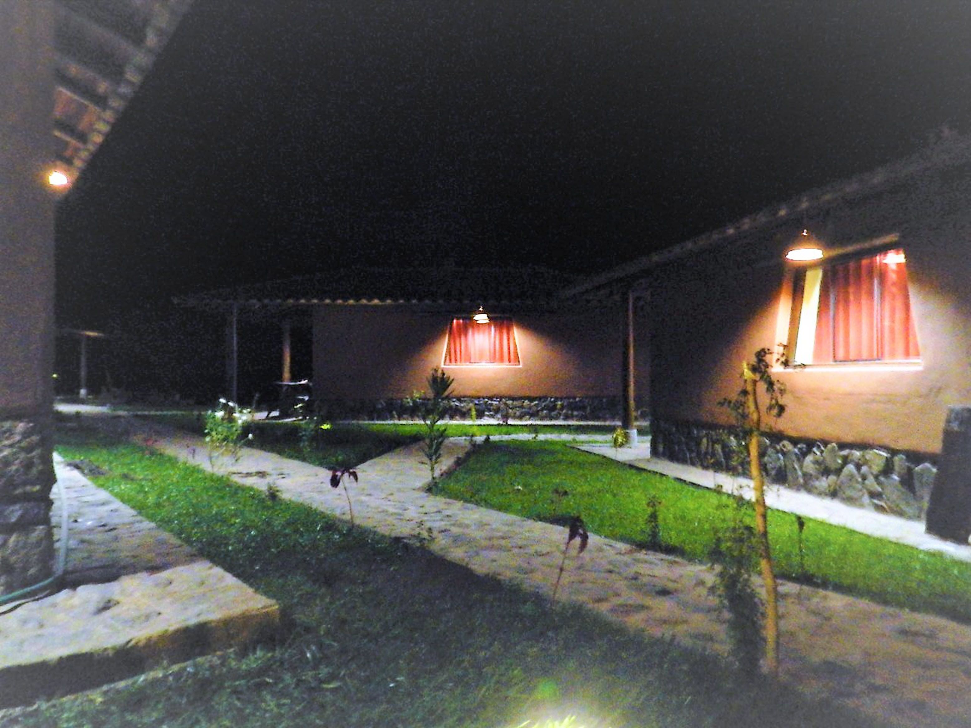 Vista nocturna de un edificio con fachada de piedra, césped cuidado y un camino que conduce a la entrada.