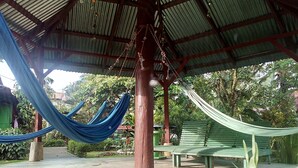 A covered outdoor area with a hammock, a bench, and a concrete floor.