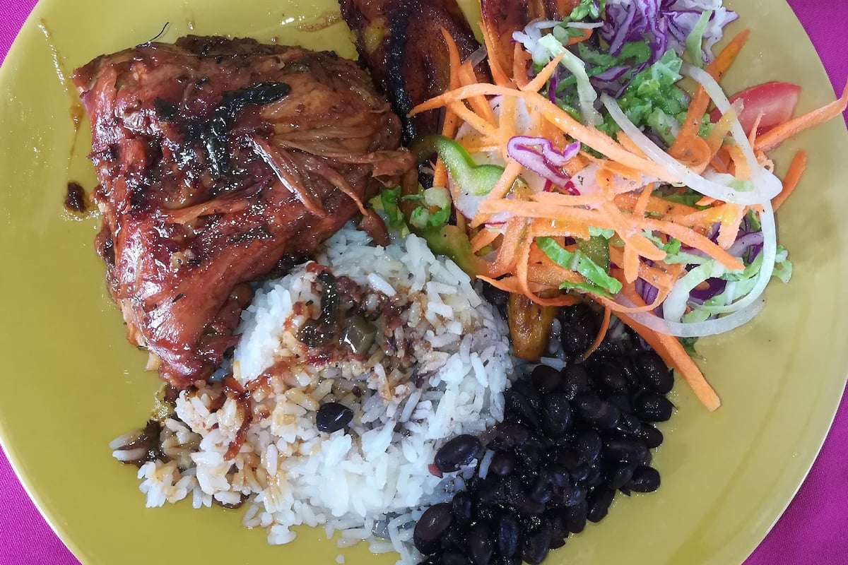 Une assiette de nourriture comprenant du riz, des haricots noirs, un morceau de viande, des bananes plantains frites et une salade.