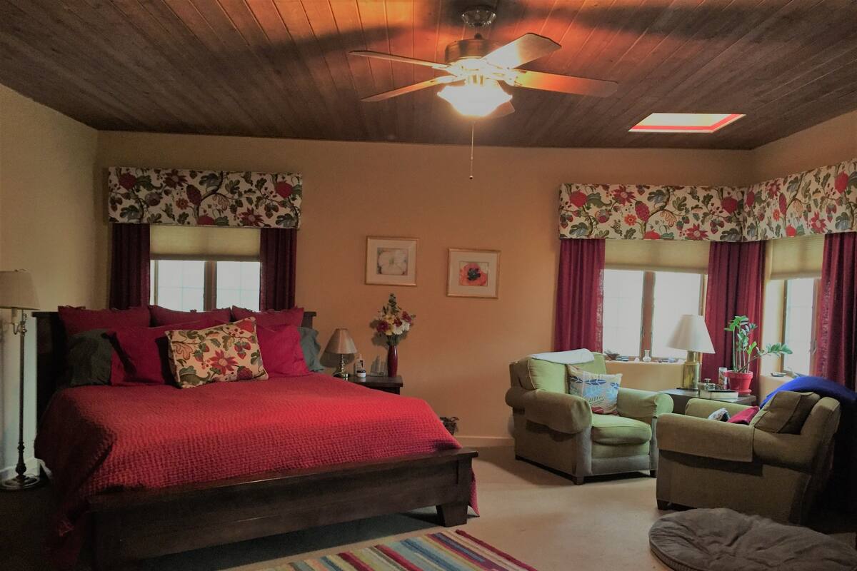 Een slaapkamer met een groot bed, twee fauteuils, een bank, een plafondventilator en bloemen gordijnen.