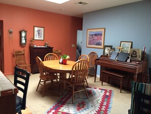 A dining room with a wooden table and chairs, a piano, and a rug.