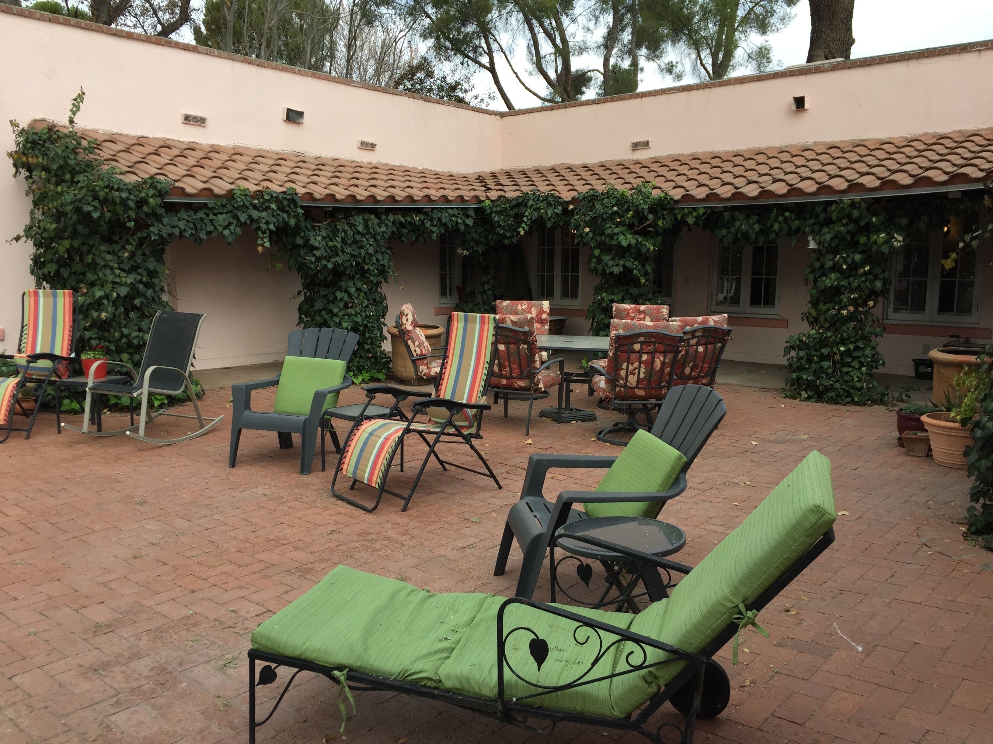An outdoor patio with brick flooring, green cushioned lounge chairs, and a table with chairs.