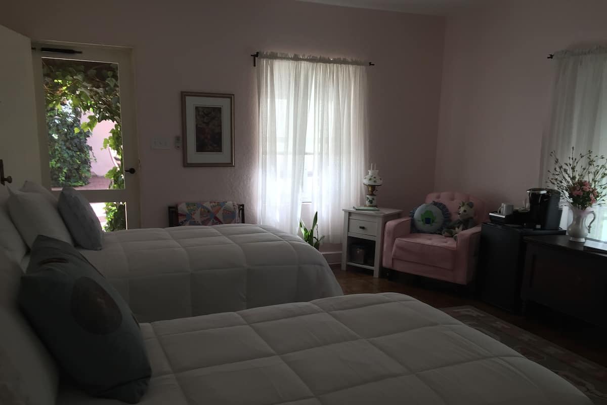 Een slaapkamer met twee bedden, een stoel, een bureau en een raam met gordijnen.