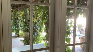 Een raam met uitzicht op een patio, inclusief een houten bankje en planten in potten.