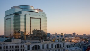 A modern glass building with a curved top, surrounded by historic architecture and a city skyline in the background. - Mini-Hotel Kievskiy (Kyiv)
