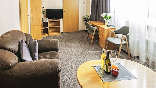 A hotel room with a brown leather sofa, a wooden desk, a television, and a dining table with chairs. - Mini-Hotel Kievskiy (Kyiv)