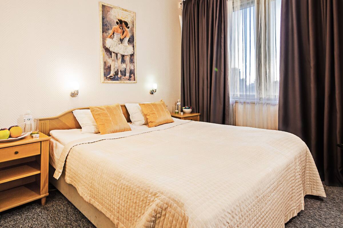 A neatly made bed with a quilted bedspread, a nightstand with a lamp, and a painting on the wall.