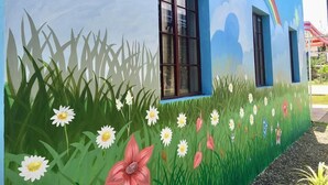 A building with a mural of a field with flowers and a rainbow.