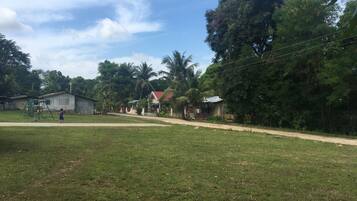 Uma área gramada com um parquinho e casas ao fundo.