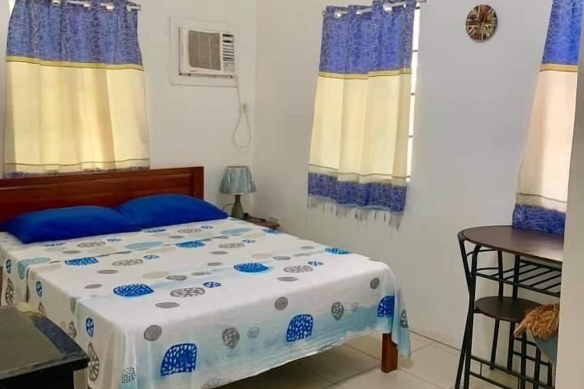 A bedroom with a bed, a desk, and two windows with curtains.