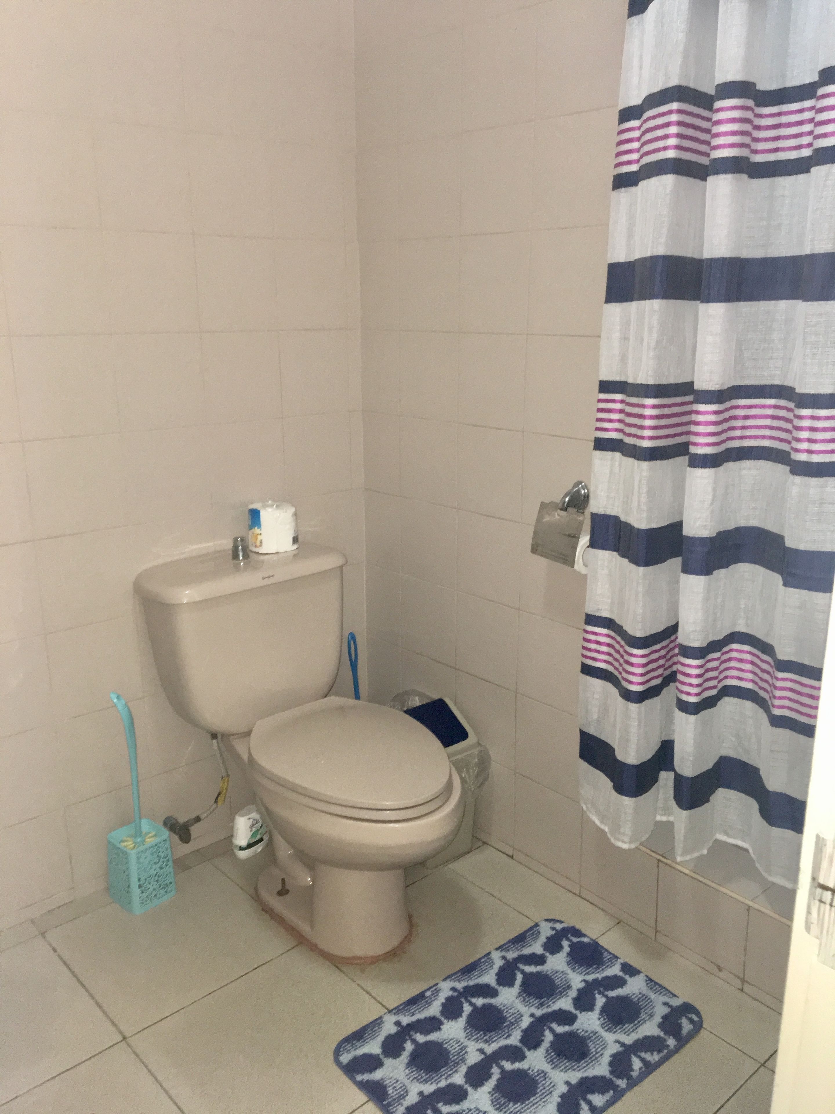 A bathroom with a toilet, a blue mat, and a striped shower curtain.