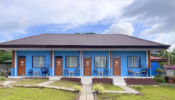 A two-story building with a tiled roof, blue exterior walls, and multiple doors. There are outdoor seating areas with chairs and tables.