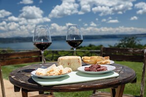 A table with cheese, meat, and wine glasses set outdoors with a lake view.