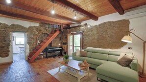 Un intérieur rustique avec un mur en pierre, des poutres en bois, un canapé vert, une table basse en bois et un escalier.