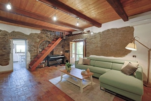A rustic interior with a stone wall, wooden beams, a green sofa, a wooden coffee table, and a staircase.
