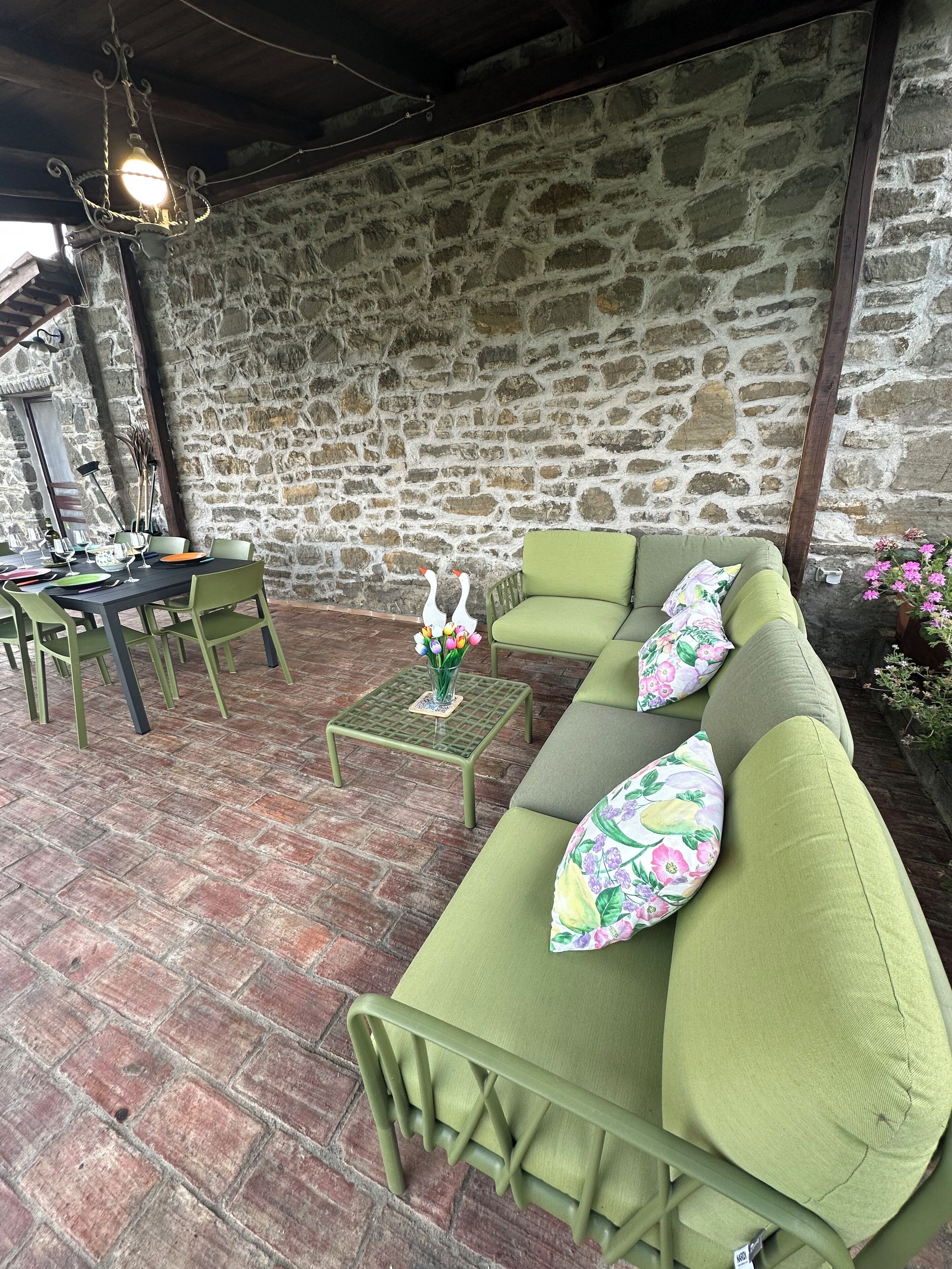 A stone-walled patio with a green sofa set, a table, and chairs.