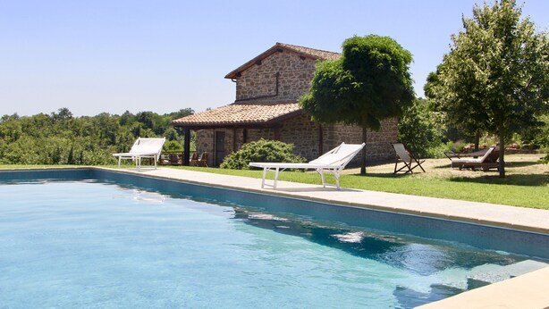 Une piscine avec des chaises longues et, en arrière-plan, un bâtiment en pierre.