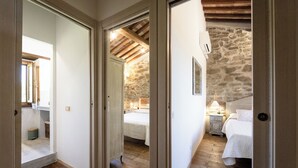 Une chambre avec un mur en pierre, des poutres en bois, un lit, des tables de chevet et une petite table de nuit.