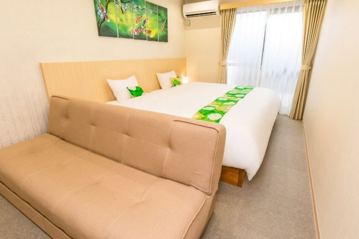 Una camera d'albergo con un letto, un divano, un quadro appeso e una finestra con tende.