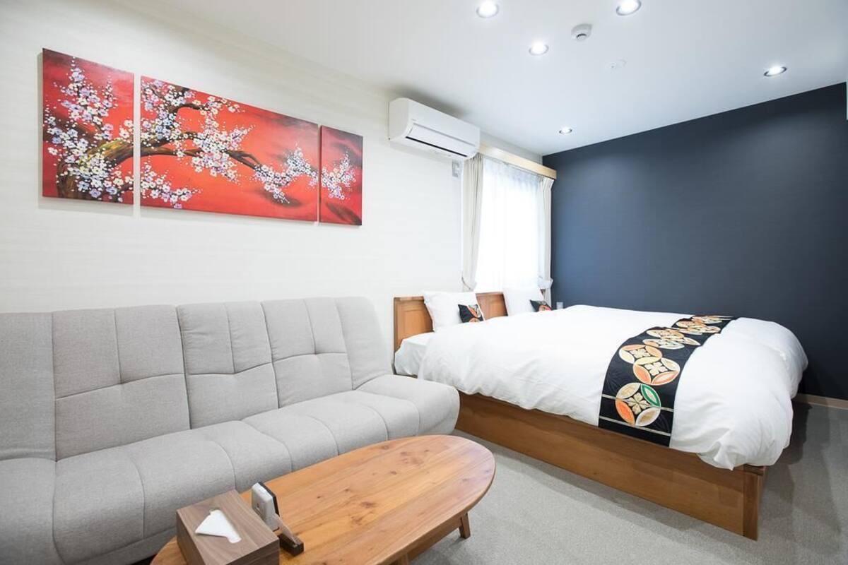 A hotel room with a bed, a sofa, a wooden side table, and two wall-mounted air conditioning units.